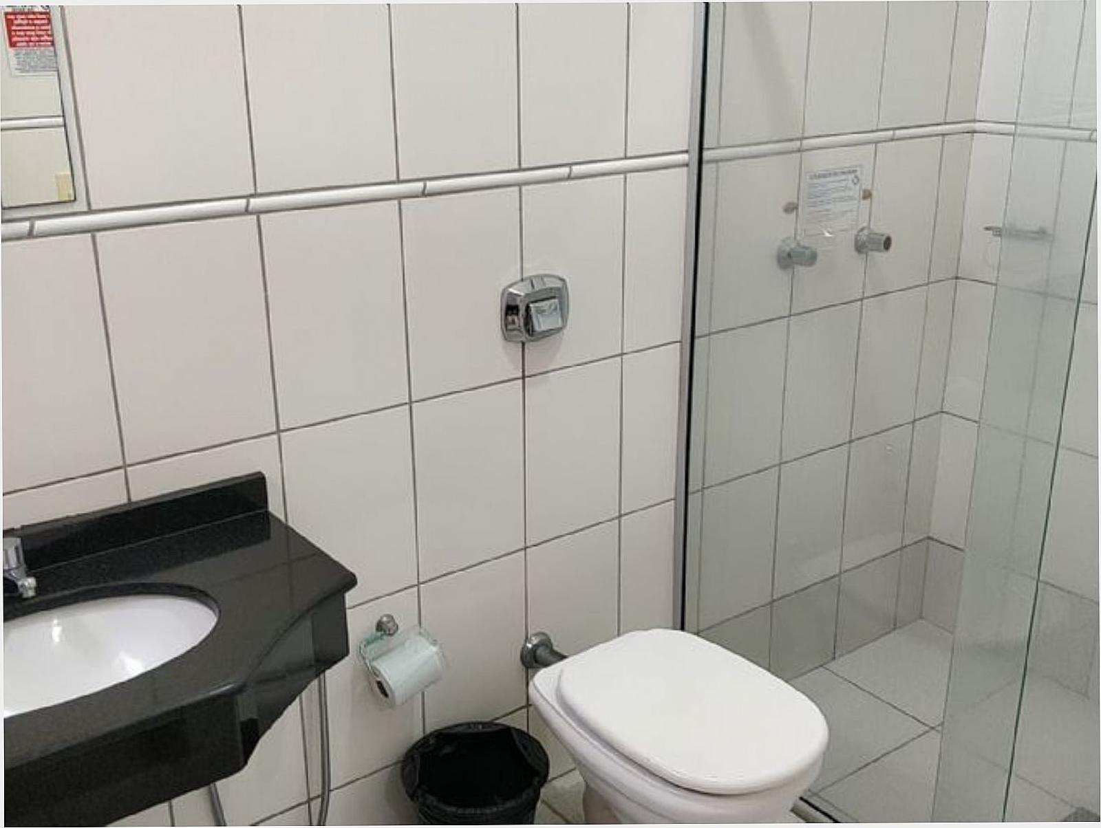 Banheiro do quarto com box de vidro, pia e revestimento branco