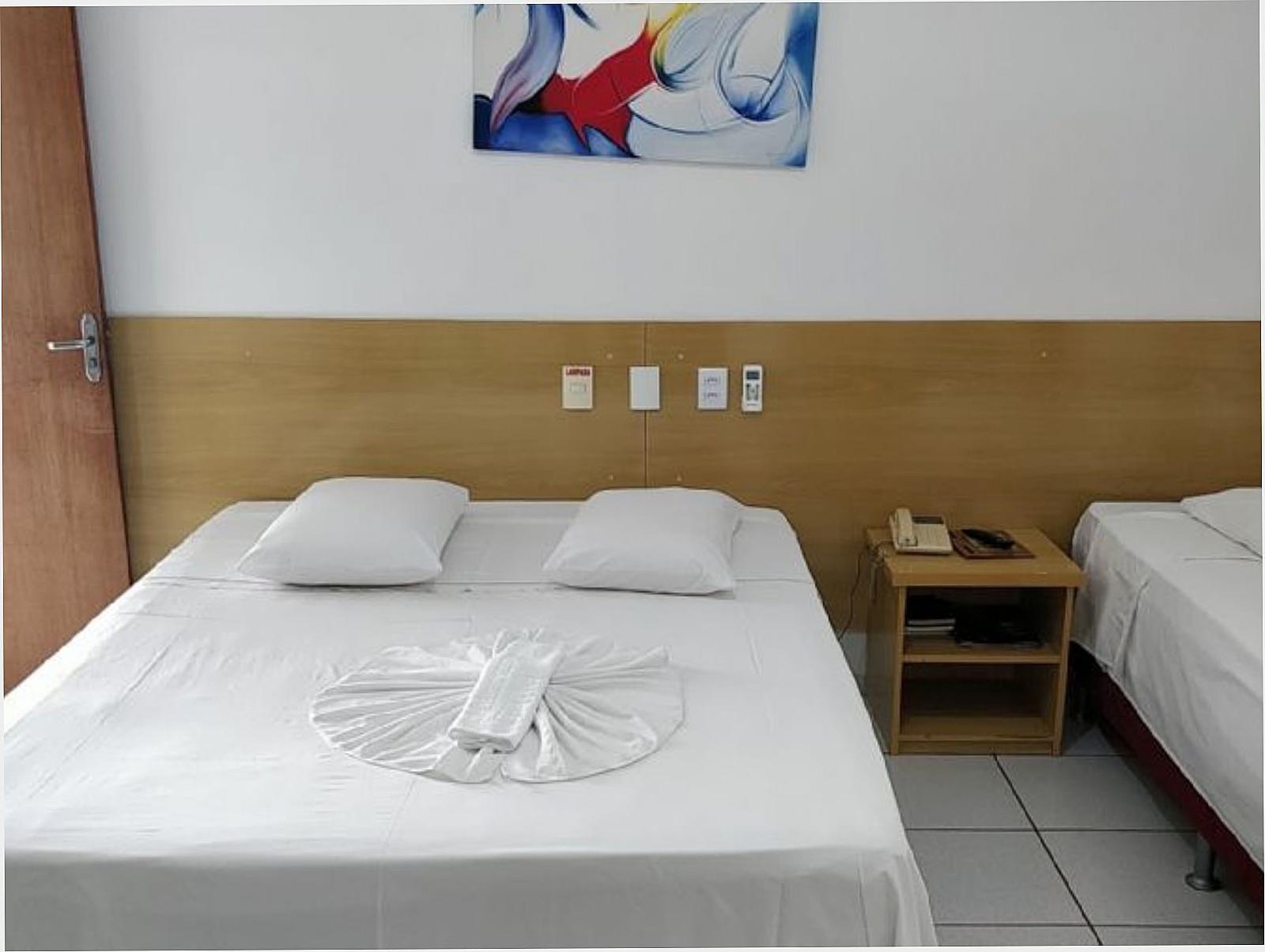 Quarto do Hotel Flor da Mata com cama de casal arrumada, cabeceira de madeira e mesa de cabeceira
