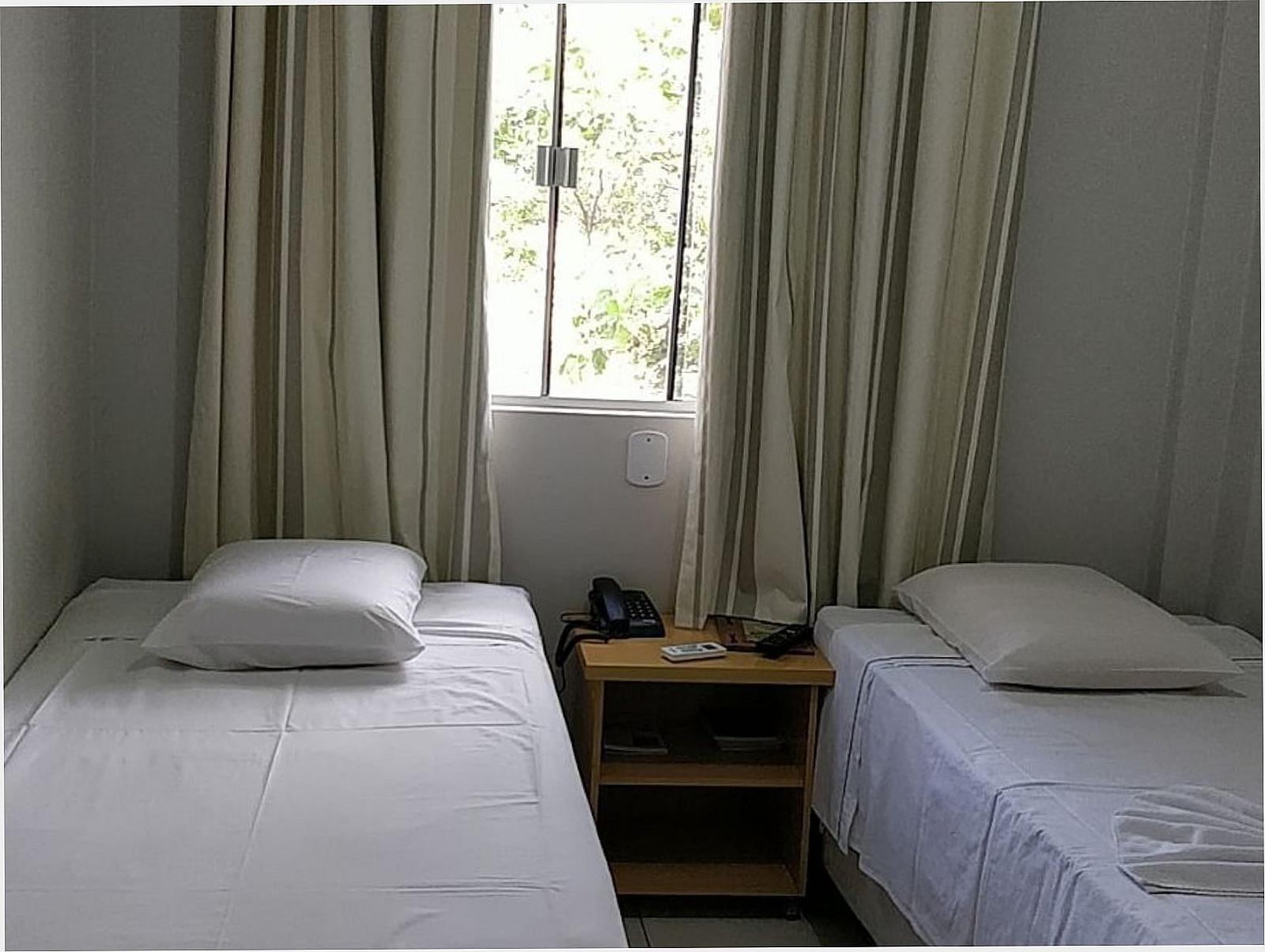Quarto com duas camas, cortinas claras e janela com luz natural